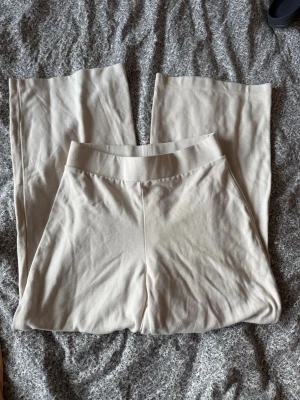 Beige mjukisbyxor från Gina Tricot - Säljer ett par beige mjukisbyxor från Gina Tricot. Byxorna har raka ben, bred resår i midjan och är gjorda i ett mjukt och stretchigt material som känns skönt mot huden. Perfekta för chill dagar hemma eller när du vill vara extra bekväm.