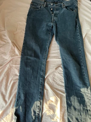 Levi's 501 - Klassiska blå Levi's 501 jeans med rak passform och knappgylf. Jeansen har fem fickor och är tillverkade i kraftig denim med kontrastsömmar. Perfekta för en avslappnad och tidlös stil.