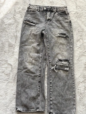 Gråa ripped straight leg jeans - Säljer ett par gråa straight leg jeans med flera slitningar och hål på benen. Jeansen är mid rise. Köpta från New yorker