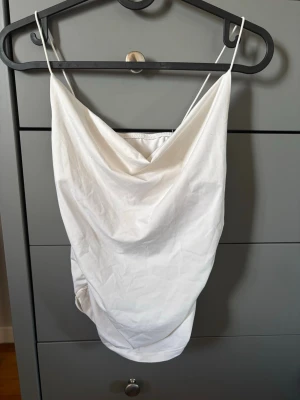 Vit linnetopp med draperad front - Snygg vit linnetopp med tunna axelband och draperad front. Perfekt till sommarens outfits och enkel att matcha med både jeans och kjol. Lätt och luftig känsla, passar dig som gillar minimalistisk stil.