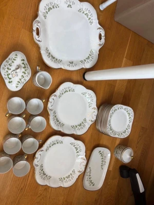 Hackefors Linnea Kaffeservis  - Hackefors Linnea kaffeservis i porslin med vita fat, koppar och serveringsfat. Grönt/rosa blommönster och guldkant. Setet innehåller 8 koppar med guldfärgade handtag, 1 stort serveringsfat,  2 mellan fat, 1 litet fat, några assietter, 1 sockerskål med lock, 1 gräddkanna och 1 större skål. Perfekt för dig som gillar vintage och detaljer.