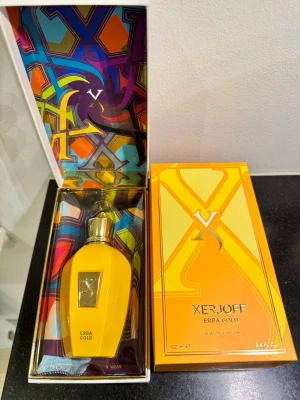 Xerjoff Erba Gold Eau de Parfum - Xerjoff Erba Gold Eau de Parfum i en lyxig, gul flaska med gulddetaljer och elegant design. Flaskan har en metallisk guldkork och en dekorativ etikett framtill. Kommer i en färgstark och exklusiv förpackning. Volym: 100 ml. Helt ny