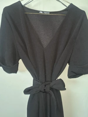 Svart omlottklänning från Zara - Svart omlottklänning från Zara med v-ringning och knytband i midjan. Klänningen har korta ärmar och en enkel, stilren design som är lätt att matcha. Perfekt för dig som gillar en klassisk look med en twist. 💕💕
