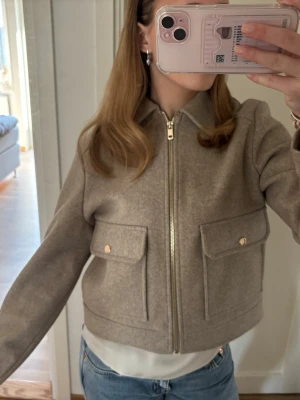 Beige jacka med fickor från Zara - Snygg beige kort jacka från Zara med två stora fickor framtill och guldfärgade knappar. Lätt att matcha med! Använd 1-2 gånger