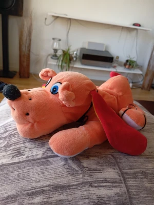 Mjukisdjur hund med röda öron - Säljer ett gulligt mjukisdjur i form av en hund. Hunden är orange med stora blå ögon, svart nos och långa röda öron med gul insida. Tillverkad i mjukt plyschmaterial och har broderade detaljer i ansiktet. Perfekt som prydnad eller kramkompis.