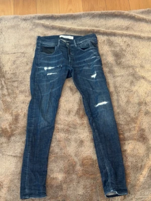 Replay denim jeans - Säljer ett par mörkblå skinny jeans från replay med slitningar och distressed detaljer framtill. Jeansen har klassisk femficksmodell, låg midja och smal passform. Materialet är stretchigt denim som sitter tajt och bekvämt.