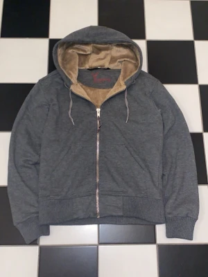 Grå hoodie  - Passar cirka 170-175 beror på vikt. Mysig grå hoodie från Elkline med dragkedja framtill och mjukt beige teddyfoder inuti tröjan. Tröjan har ribbade muddar vid ärmslut och nederkant samt justerbara snören i huvan. Perfekt för chill dagar och streetwear-stil.