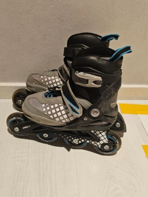 Svarta och grå inlines med blå detaljer - Säljer ett par inlines i svart och grått med blå detaljer. De har justerbara spännen, mesh-tyg för ventilation och fyra hjul per sko. Perfekta för dig som gillar att åka snabbt och smidigt på asfalt. Stl 29-33