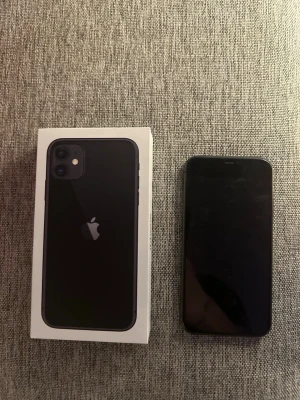 Svart iPhone 11 med originalkartong - Säljer en svart iPhone 11 från Apple. Telefonen har en stilren design med rundade hörn, glasbaksida och dubbla kameror på baksidan. Kommer med originalkartong. Perfekt för dig som vill ha en snygg och kraftfull smartphone.