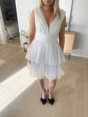 Vit omlottklänning med volang - Säljer en vit kortklänning med omlottdesign och v-ringning. Klänningen har flera lager av tunn, luftig tyll och markerad midja. Ärmlös modell som ger en romantisk och elegant känsla. Perfekt för sommarens alla tillfällen och speciellt studentklänning.💕Tag is on.