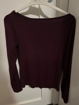 Mörklila långärmad topp från NewYorker - En enkel och stilren mörklila långärmad topp från NewYorker. Toppen har en rundad halsringning och är gjord i ett mjukt material som sitter skönt mot kroppen. Perfekt att matcha med jeans eller kjol för en clean look. Tröjan är i storlek M.