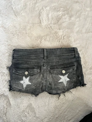 Svarta jeansshorts med stjärnor  - Coola svarta jeansshorts med slitna detaljer och råa kanter. Baksidan har två fickor med vita stjärnor. Jag har gjort om dom ganska mycket. 