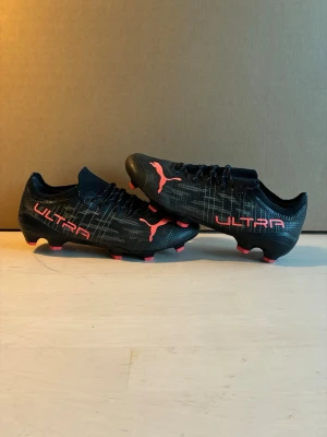 Puma Ultra fotbollskor  - Säljer ett par puma ultra fotbollskor i svart med ljus röda detaljer. Bra skick dobbar och liknande intakt. Storlek 42/5. Har mindre defekter på utsidan av skorna (Se sista bilden) därav lite billigare pris. Köpta för 1800. Pris kan diskuteras!