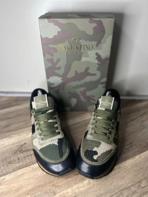 Valentino Rockrunner sneakers camouflage - Snygga Valentino Rockrunner sneakers i grönt, beige och svart med camouflage-mönster. Skorna har snörning, detaljer i mocka och skinn samt coola nitar på hälen. Perfekta för dig som vill sticka ut med exklusiva dojjor. Skorna är använt sparsamt så ej mycket slitage på sulan alls. Box med kommer har du frågor hör av dig priset kan alltid diskuteras.