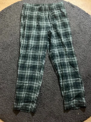 Rutiga pyjamasbyxor från H&M - Mysiga pyjamasbyxor från H&M i grönt och vitt rutigt mönster. Byxorna har rak passform och resår i midjan för extra komfort. Perfekta för chillkvällar hemma. Tillverkade i mjukt tyg som känns skönt mot huden. Nästa aldrig använt.