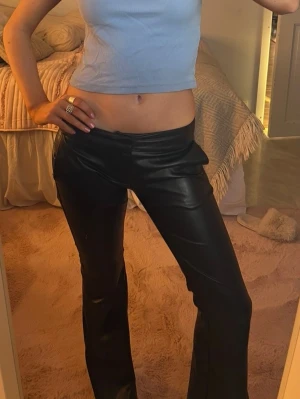 Svarta skinnbyxor  - Säljer ett par svarta byxor i fuskskinn med utsvängda ben. Byxorna har låg midja och är i storlek S från Bershka. ÄLSKAR DESSA men har tyvärr blivit för små❤️❤️🥹🥹