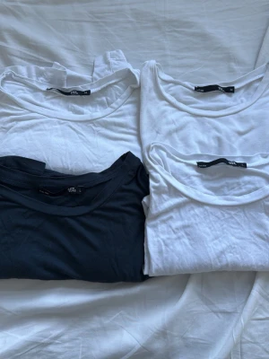 Basic vita och mörkblå t-shirt - Fyra basic t-shirts från lager 157, tre vita och en svart. Alla har rund halsringning och korta ärmar. Perfekta att matcha till jeans eller shorts. Tillverkade i mjuk bomull för skön känsla hela dagen. Storlekarna M, M, L & L