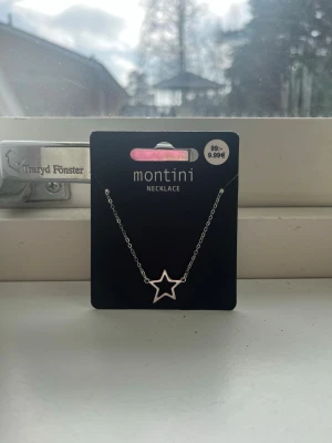 Silverfärgat halsband med stjärna - Helt nytt snyggt halsband från Montini med en tunn silverfärgad kedja och ett öppet stjärnformat hänge. Perfekt för dig som gillar minimalistiska smycken med en trendig touch. Märkt med Ur & Penn på baksidan av förpackningen.