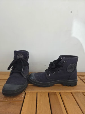 Palladium - Säljer ett par svarta sneakers från Palladium med slitstark textil, grov gummisula och snörning. Skorna har logga på sidan och plösen samt metallöljetter för snören. Använd fåtal gånger. Så gott som nya.
