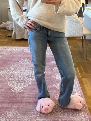Blå raka/baggy jeans med låg midja - Säljer ett par klassiska blå jeans med rak passform och låg midja. Jeansen har fem fickor, bälteshällor och stängs med knapp och dragkedja. Perfekta till vardags och lätta att matcha med olika stilar.