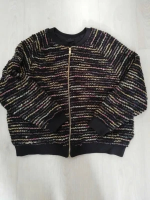 Randig teddyjacka med dragkedja - Mysig teddyjacka i svart med färgglada ränder i beige, lila och gult. Jackan har en rak passform, ribbade muddar och dragkedja framtill. Perfekt för dig som vill ha en unik och trendig look. Materialet är fluffigt och ger en cool textur. från h&m och storlek S! köpt för 500, nypris är 350 och knappt använd!