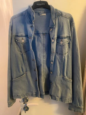 Ljusblå jeansjacka  - Snygg ljusblå jeansjacka  med klassisk rak passform. Jackan har två bröstfickor med knapp, två sidofickor och silverfärgade knappar framtill. Tillverkad i mjukt denimtyg och har en ståkrage för en modern touch.