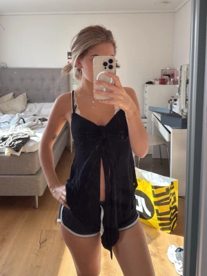 Svart linnetopp med knyt och v-ringning - Svart linnetopp med smala axelband, djup v-ringning och snygg knytning framtill. Toppen är ärmlös och har en loose passform, perfekt för varma sommardagar. Tillverkad i ett mjukt och lätt material.