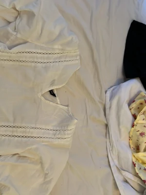 Vit blus med spetsdetaljer - Söt vit blus med raka spetsdetaljer framtill och vid ärmarna. Blusen har en avslappnad passform och rundad halsringning. Perfekt för en stilren och enkel look.