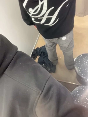 Svart hoodie med vit logga - Säljer en svart hoodie med stor vit grafisk logga på ryggen. Hoodien har huva och en avslappnad passform, perfekt för en streetwear-look. Materialet ser ut att vara mjukt och bekvämt, troligen bomullsblandning.