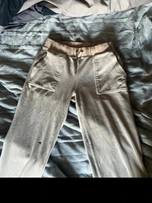 Beige mjukisbyxor med fickor - Säljer ett par beige mjukisbyxor med bred resårmidja och dragsko. Byxorna har stora framfickor och bakfickor med knappdetaljer. Tillverkade i mjukt material som är skönt att ha på sig. Är dock lite brännmärken på benet se blid 4-5