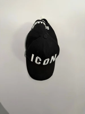 Svart ICON keps från Dsquared2 - Säljer en svart keps från Dsquared2 med stor, vit broderad text 'ICON' framtill och Dsquared2-broderi baktill. Klassisk böjd skärm och justerbar rem bak. Perfekt för dig som vill ha en skön o fet keps
