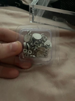 Silverfärgade berlocker och smyckesdelar - Ett set med små silverfärgade berlocker och smyckesdelar i olika former, perfekta för att skapa egna smycken eller accessoarer. Innehåller bland annat runda och hexagonala delar samt små öglor. Levereras i en plastask.