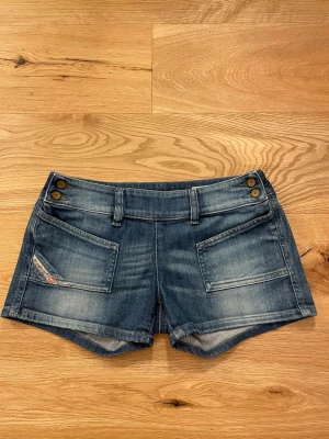 Blå jeansshorts från Diesel!! 💖 - Snygga blå jeansshorts från Diesel med slitna detaljer, två stora framfickor och två bakfickor. Shortsen har bälteshällor, dekorativa knappar framtill och en klassisk Diesel-patch bak i midjan. Perfekta för varma dagar!