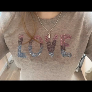 Zadig voltier tröja - Snygg beige tröja med texten LOVE i glittriga stenar i blått, lila och rosa på bröstet. Rund halsringning och mjukt material som känns skönt mot huden. Perfekt för dig som vill ha en enkel men ändå unik look.