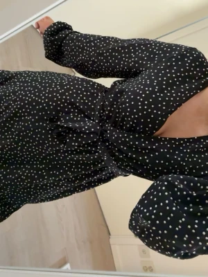 Svart prickig klänning  - Snygg svart kortklänning med vita prickar och omlottmodell. Klänningen har v-ringning, långa ärmar med resår vid handlederna, säljer pågrund av att jag aldrig använt den 