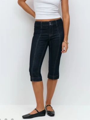 Mörkblå denim capri shorts - Snygga mörkblå denim capri shorts med kontrastsömmar och uppvikta benslut. Modellen har hög midja och klassisk femficksdesign. Perfekta för en avslappnad och trendig sommarlook.