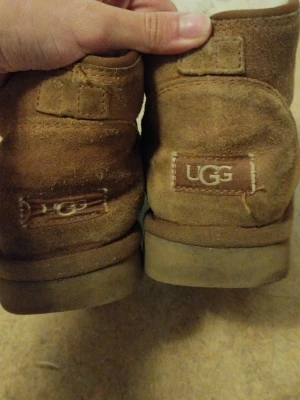 Bruna UGG boots i mocka - Klassiska bruna UGG boots i mjuk mocka med fårskinnsfoder. Modellen är ankelhög och har rund tå samt bred passform. UGG-logga bak på hälen. Perfekta för kalla dagar när du vill ha det riktigt bekvämt och varmt om fötterna. Säljer billigt för att jag vill bli av med dem