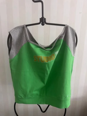 Grön och grå linnetopp från Nike - Sportig linnetopp från Nike i grön och grå färg. Toppen är ärmlös och har en enkel, clean design med Nike-logga broderad framtill. Perfekt för träning eller en avslappnad look. Tillverkad i mjuk bomull för skön känsla.