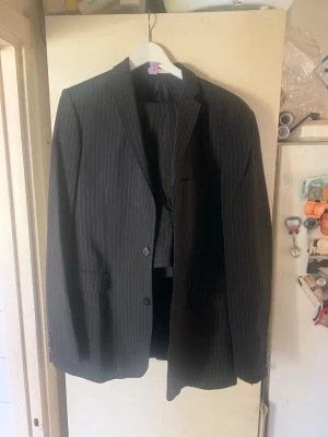 Svart randig kostym Johan Lindeberg med klassisk passform - Säljer en svart kavaj med tunna vita ränder från märket johan Lindeberg Kavajen har klassisk passform, två knappar framtill och fickor med lock. Perfekt för dig som vill ha en stilren och tidlös look.