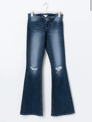 Blå bootcut jeans med slitningar - Bootcut jeans i mörkblå denim med slitningar på knäna och fransad midja. Jeansen har klassisk femficksdesign och en snygg tvätt med ljusare partier. Perfekt för dig som gillar en trendig och avslappnad look.