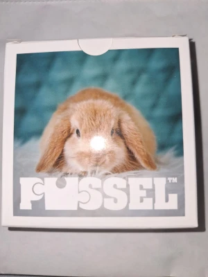 Pussel med kaninmotiv - Säljer ett pussel från FUSSEL med ett gulligt motiv av en ljusbrun kanin mot en blå bakgrund. Pusslet består av flera bitar och kommer i en vit ask med samma bild på locket. Perfekt för dig som gillar söta djur och pyssel.
