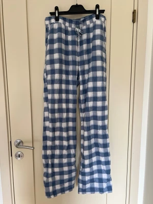 Rutiga pyjamasbyxor i blått och vitt - Mjuka pyjamasbyxor med blåvitt rutmönster och snöre i midjan. Byxorna har raka ben och fickor.