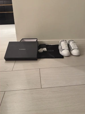 Vita och grå sneakers från Numeris - Snygga sneakers från Numeris i vitt och grått med coolt mönster på sidan. Skorna har vita tjocka snören, rund tå och ovandel i textil och läder. Kommer med extra skosnören och dustbag. Perfekta för dig som vill ha en clean och trendig look.