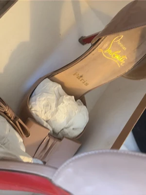 Beige pumps från Christian Louboutin - Säljer ett par eleganta beige pumps från Christian Louboutin med ikonisk röd undersida. Skorna har öppen tå och en snygg rosett framtill. Tillverkade i läder och har en klassisk, stilren design som passar perfekt till många outfits.