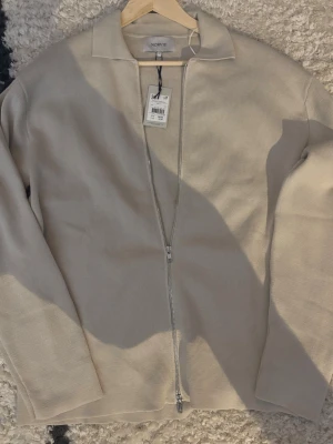 Beige ziptröja från Norvie  - Snygg beige ziptröja från Norrtill med krage och tvåvägsdragkedja helt oanvänd med nypris på 799. Tröjan har en stilren och minimalistisk design i ett mjukt stickat material. Perfekt för dig som gillar enkel och clean stil.