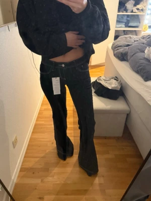 Svarta bootcut jeans med vit söm - Säljer ett par svarta bootcut jeans med markerade vita sömmar och klassisk femficksdesign. Jeansen har låg midja och vida ben, vilket ger en snygg retrostil. Materialet är denim med stretch för extra komfort. Perfekta för dig som gillar trendiga siluetter.