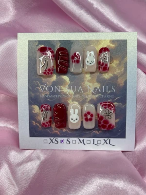 CherryMiffy (S);Short Square - Handgjorda press-on naglar i rött och nude med vita kaniner (Miffy) och silvriga detaljer. Setet har söta kaninmotiv(Miffy) , blommor och abstrakta mönster. Naglarna har en blandning av glansig finish och 3D-effekter. Perfekt för dig som vill ha unika och kreativa naglar.S: 15 mm, 11,5 mm, 12 mm, 11 mm, 9 mm 