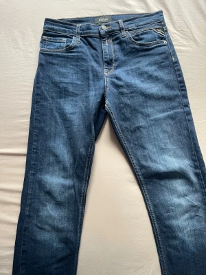 Replay - Säljer ett par klassiska blå jeans från Replay med rak passform och fem fickor. Jeansen har snygga slitningar och kontrastsömmar, samt en traditionell knappgylf. Perfekta för dig som gillar tidlös denimstil. Passar s-m.