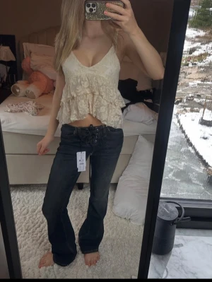 Beige spetsig volangtopo - Söt beige spetstopp med tunna axelband och v-ringning. Toppen har flera lager volanger i spets och ger en romantisk vibe. Perfekt att styla med jeans eller kjol för en trendig look. Aldrig använd från zara köpt förra året💘