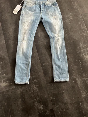 Dondup jeans slim fit - Säljer ett par lite schystare ljusblå jeans med raka ben och slitningar på både fram- och baksida. Jeansen har klassisk femficksdesign och är tillverkade i denim. Perfekta för en avslappnad och trendig look. Pris går att diskuteras pris ej hugget i sten